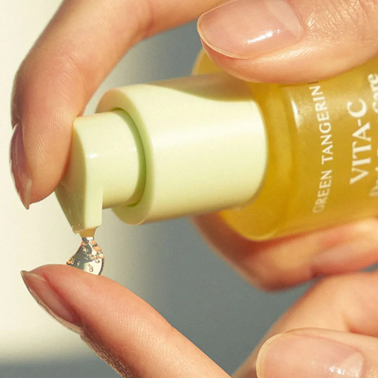 Hand holding a bottle of skincare product with a droplet on a reflective surface